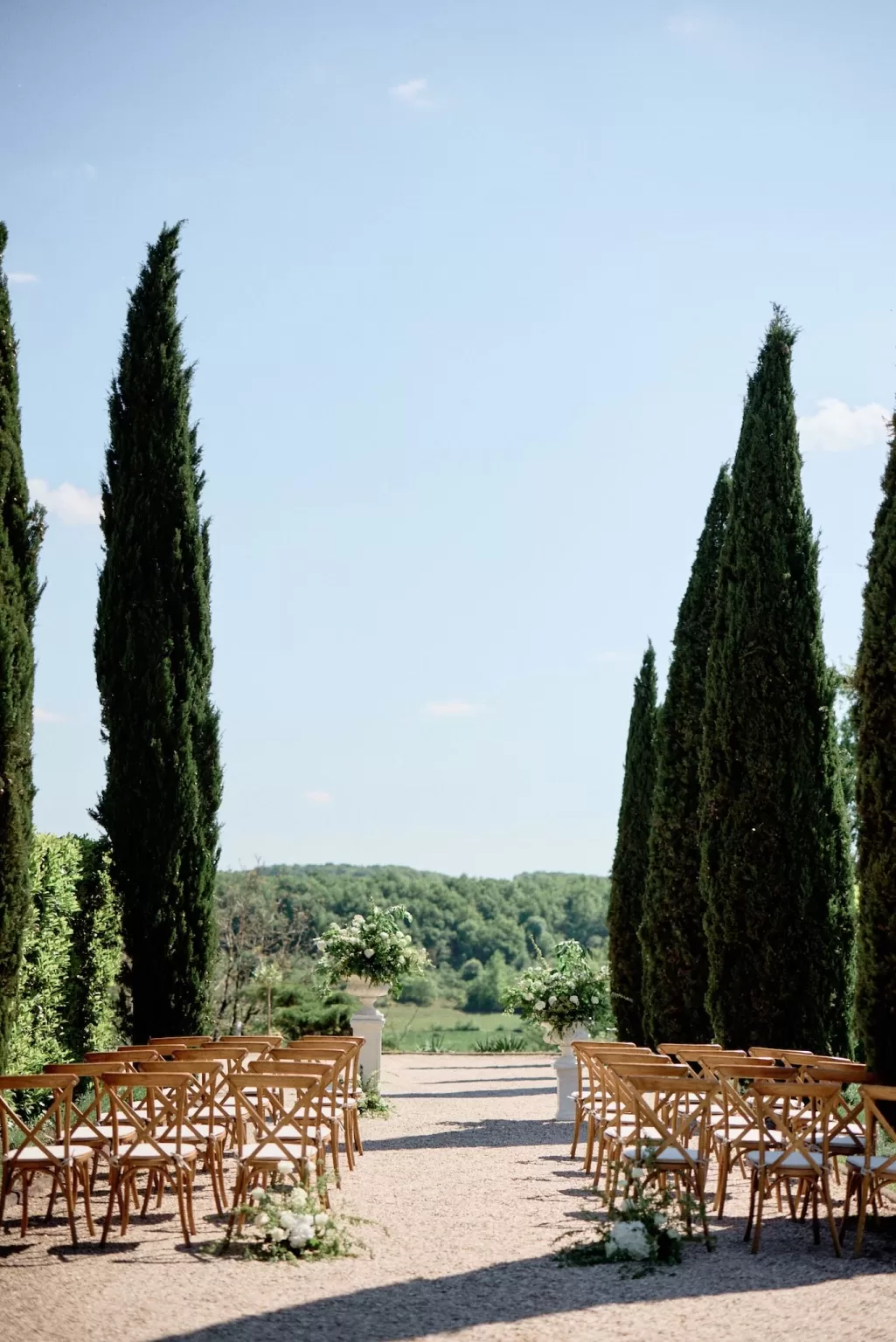 Outdoor ceremony aisle at Chateau de Sanse framed by cypress trees and views of the Dordogne countryside.
