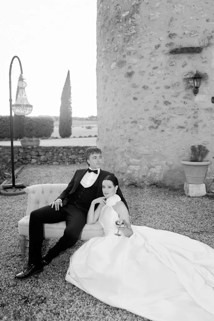 Editorial black-and-white portrait of bride and groom beside château stone wall.