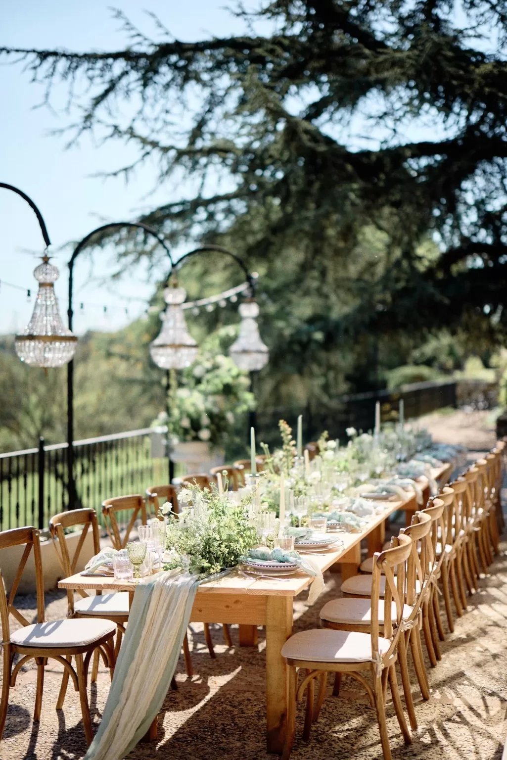 Long outdoor reception table under chandeliers and greenery at Chateau de Sanse.