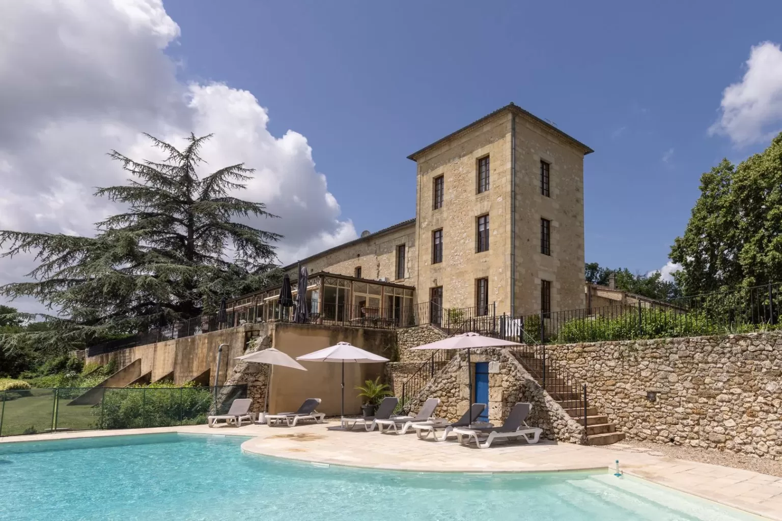 Sun loungers and parasols by the pool with château and pine trees in the background at Château de Sanse