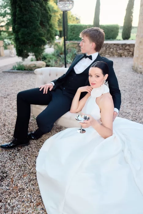 Bride and groom reclining on vintage loveseat in the garden at Château de Sanse.