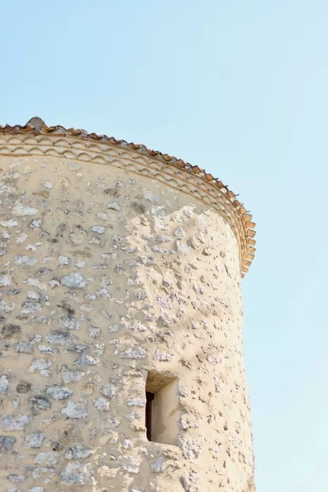 Stone tower with terracotta roof tiles against a clear blue sky at Chateau de Sanse.