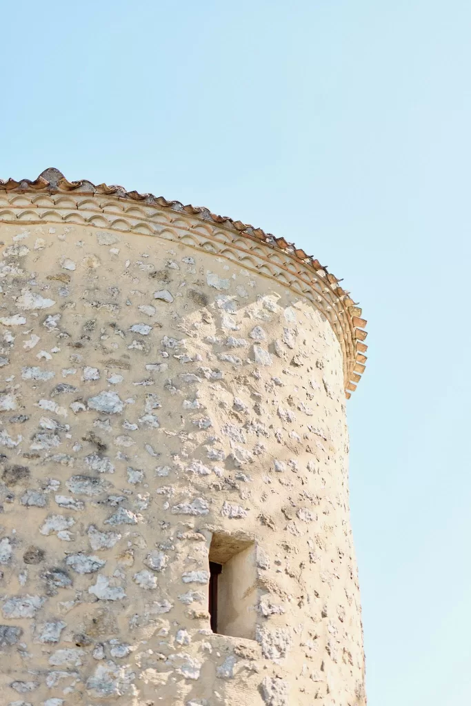 Stone tower with terracotta roof tiles against a clear blue sky at Chateau de Sanse.