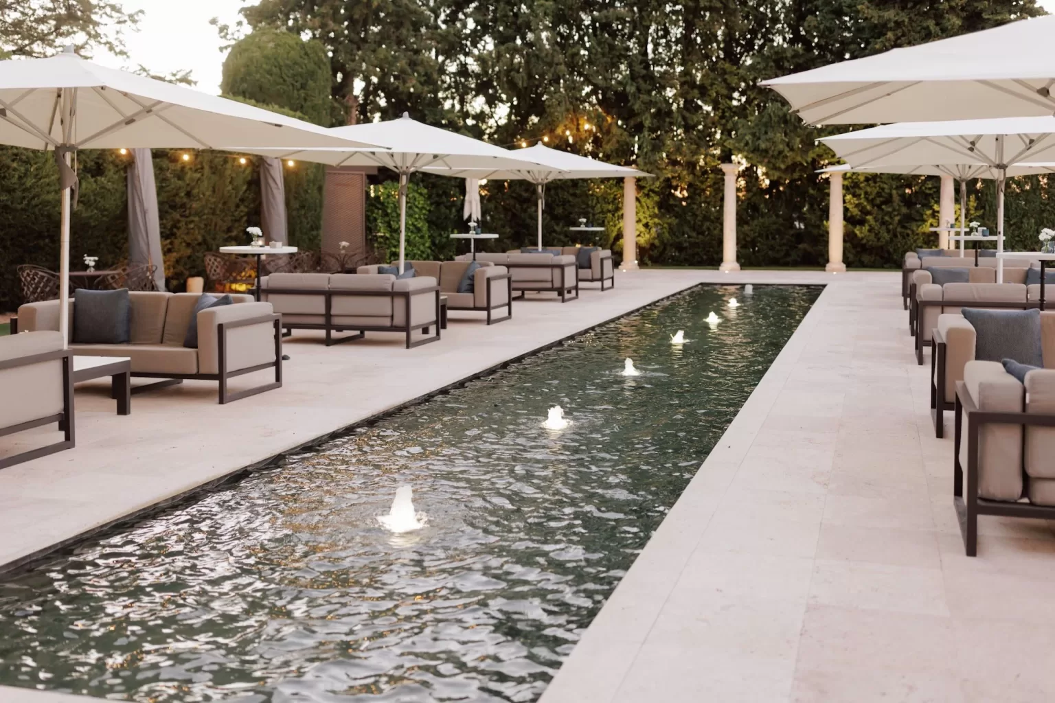 Elegant outdoor lounge by the lit water feature at Cigarral de las Mercedes, styled for an evening wedding reception.