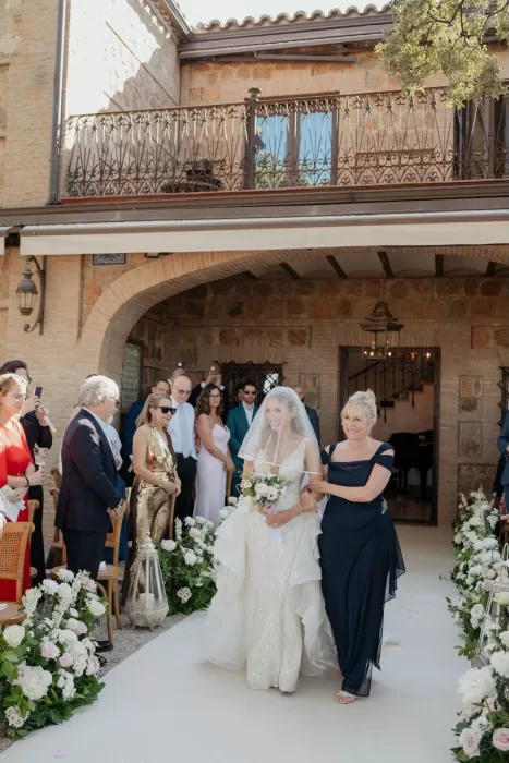 Bride walks down the aisle with her mother, surrounded by floral arrangements at Cigarral de las Mercedes.