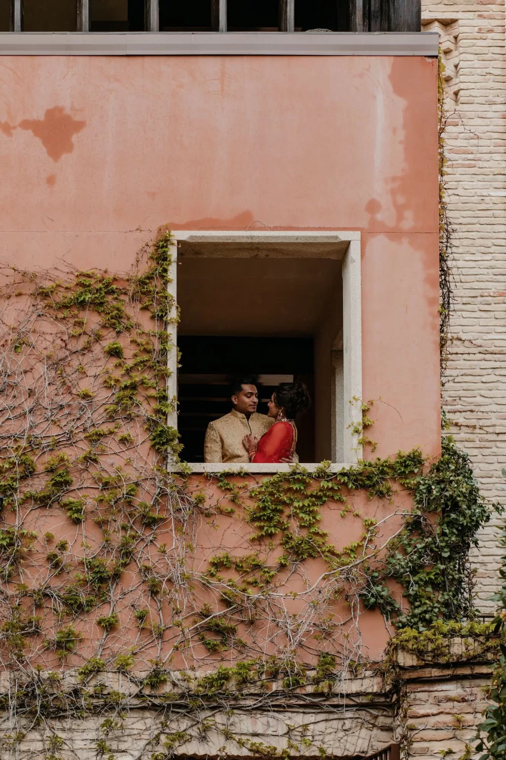Romantic moment between the couple framed in a terracotta balcony with ivy at Cigarral de las Mercedes.