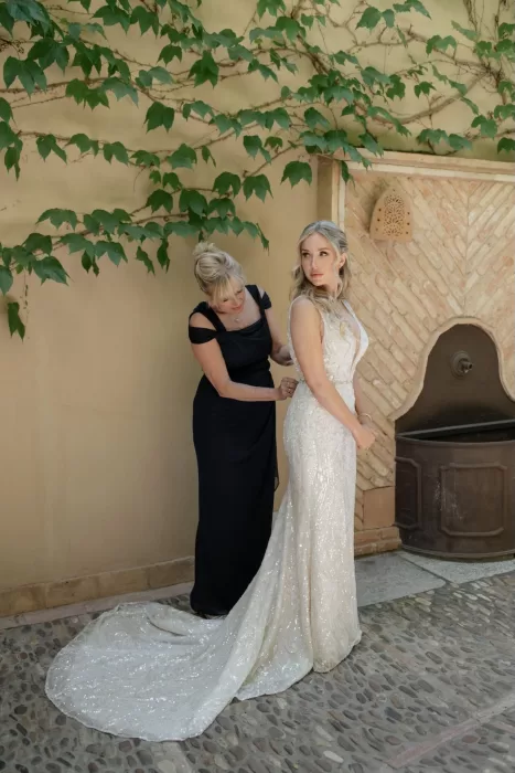 Bride gets help with her dress beside a vine-covered wall at Cigarral de las Mercedes.