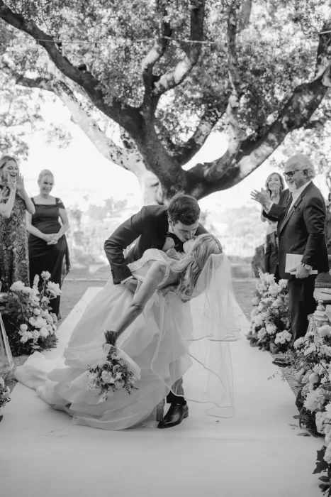 Groom dips the bride for a celebratory kiss under the trees at the end of the ceremony at Cigarral de las Mercedes.