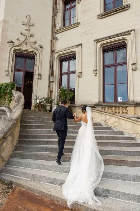 Bride and groom ascending stone steps toward Château Challain’s ornate entrance.