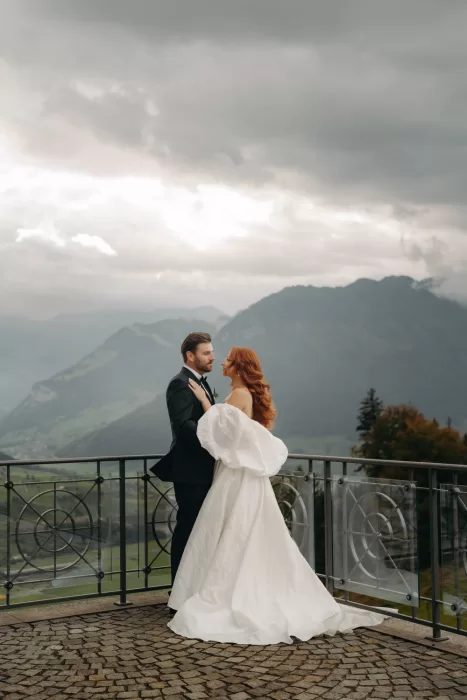 Bride and groom gaze at each other on the balcony of Hotel Villa Honegg, with dramatic alpine scenery behind them.