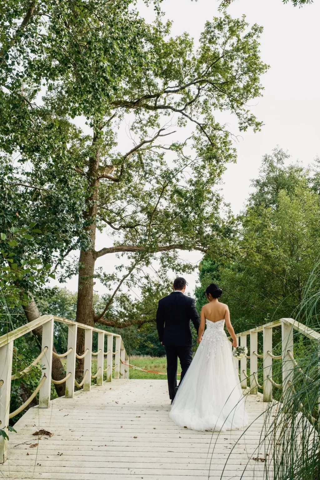 Couple walking across a wooden bridge surrounded by lush trees at Château Challain.