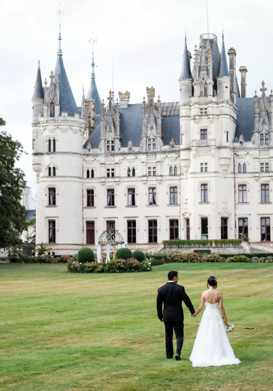 Newlyweds walking toward Château Challain’s gardens hand in hand.
