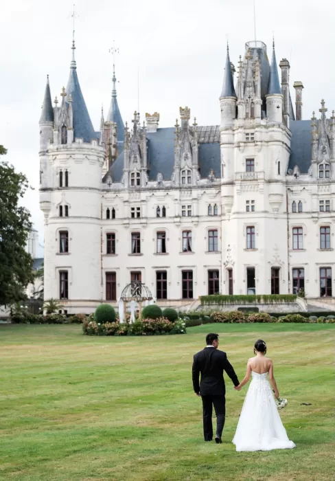 Newlyweds walking toward Château Challain’s gardens hand in hand.