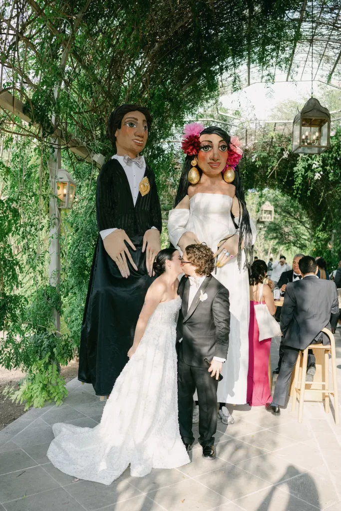 Bride and groom kiss beneath traditional Mexican giant puppets during wedding celebration at Luna Escondida.