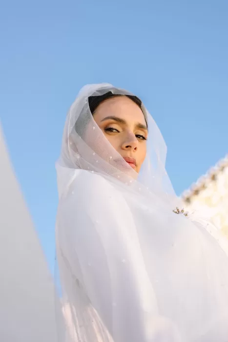 Dramatic portrait of bride beneath pearl-studded veil with blue sky backdrop at Masia Cabellut