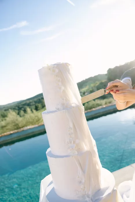 Close-up of a knife cutting into the textured white wedding cake by the pool at Masia Cabellut.
