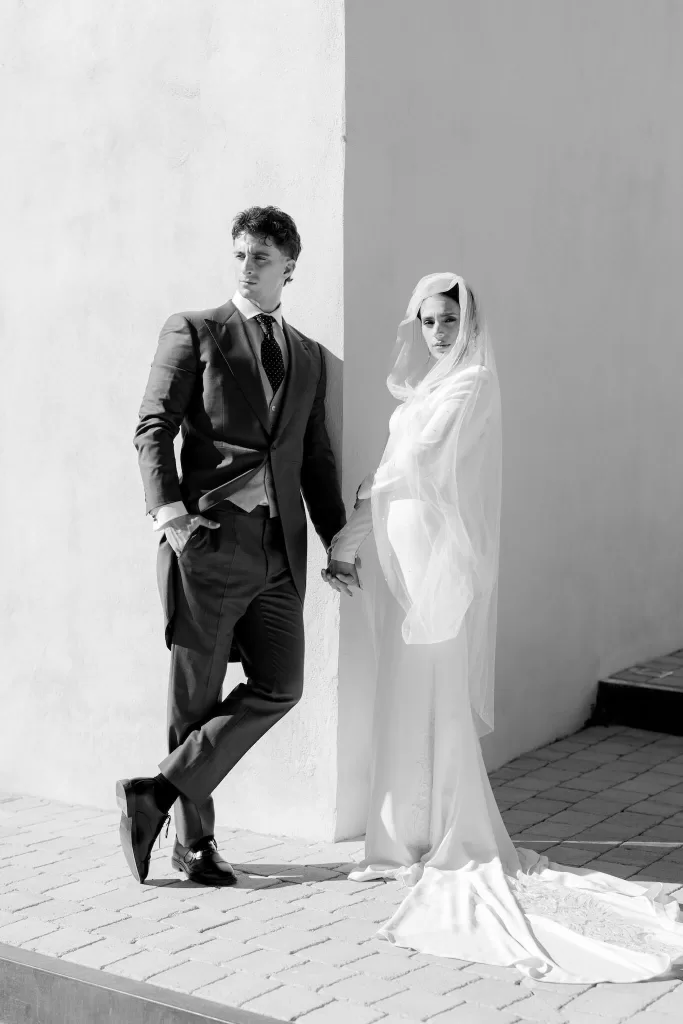 Bride in long-sleeved gown and veil holding hands with groom in a modern architectural corner at Masia Cabellut.