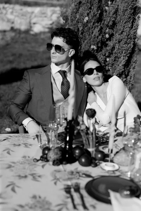 Bride and groom in sunglasses leaning back at a chic al fresco table at Masia Cabellut, exuding modern editorial style.