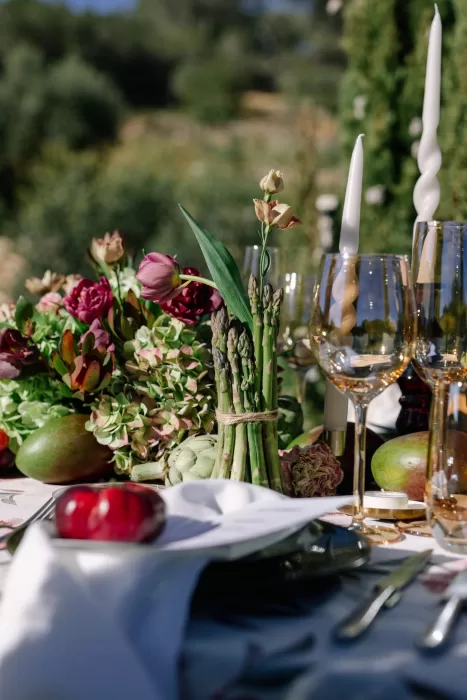 Close-up of a wedding table at Masia Cabellut with asparagus bundle, tulips, and golden glassware for a modern floral display.