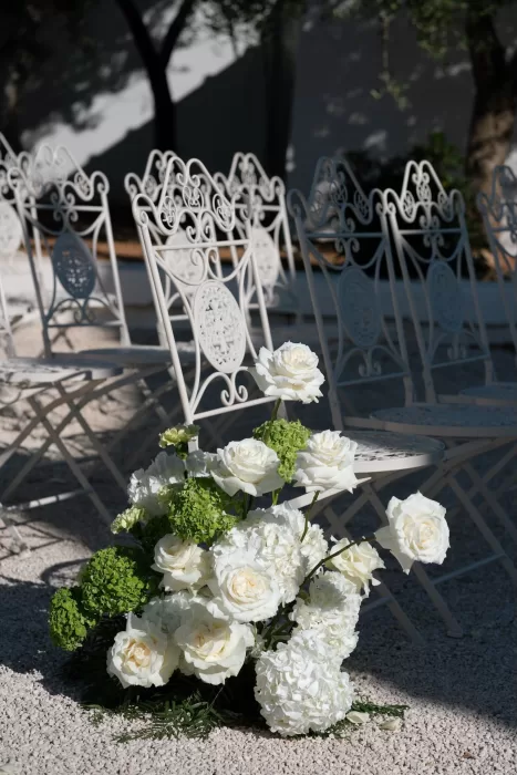 Close-up of white and green ceremony flowers beside vintage wrought iron chairs at Masseria San Giovanni.