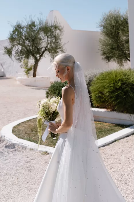 Bride with flowing veil and bouquet under soft sunlight at Masseria San Giovanni