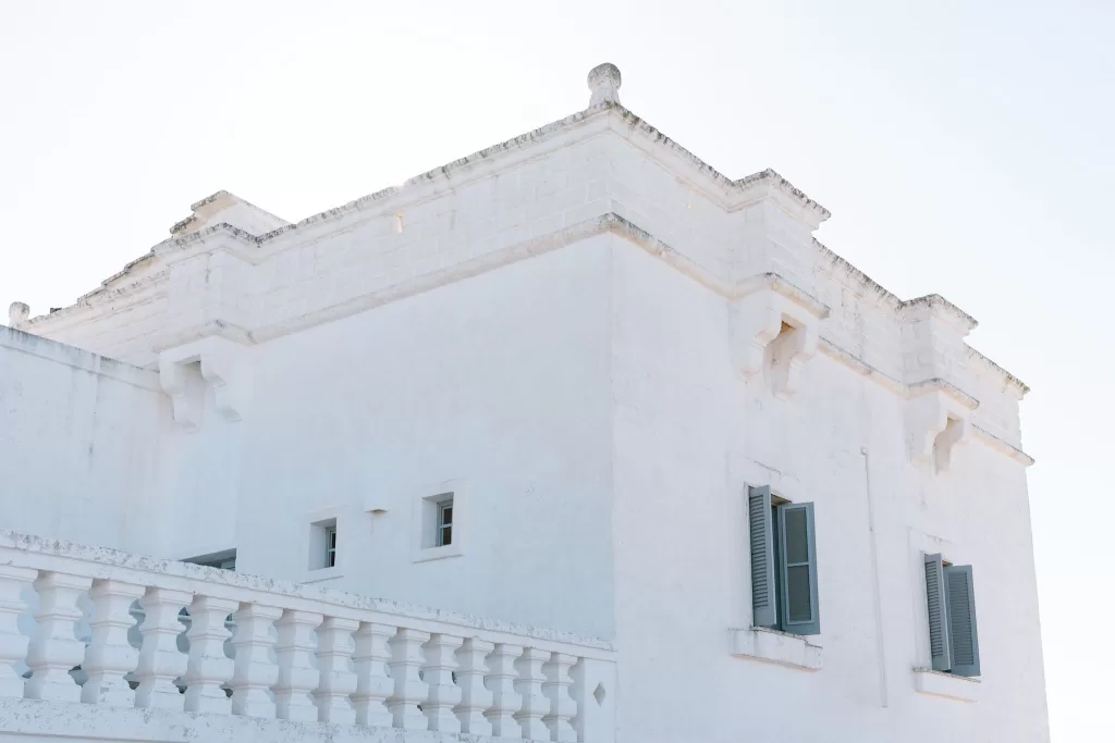 Bright, minimalist façade of Masseria San Giovanni with traditional Puglian architecture and open shutters.