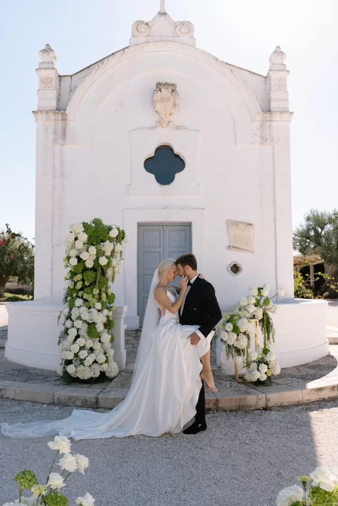 Romantic moment between newlyweds in front of the chapel at Masseria San Giovanni, framed by cascading floral columns.