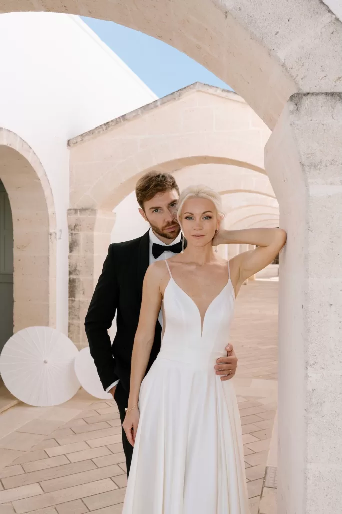 Groom holds bride close in a romantic moment beneath arched walkway at Masseria San Giovanni
