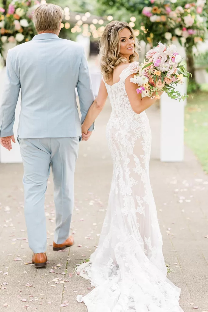 Bride looking back while holding groom’s hand, surrounded by petals at Monte Pacis