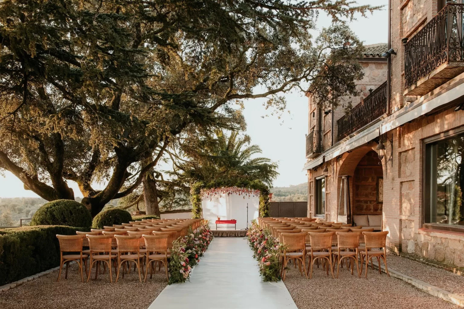 Elegant outdoor ceremony setup beneath trees with floral aisle at Cigarral de las Mercedes.