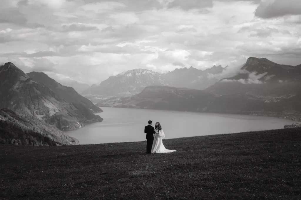 Bride and groom stand together in a vast mountain landscape near Hotel Villa Honegg, facing the lake and peaks in the distance.