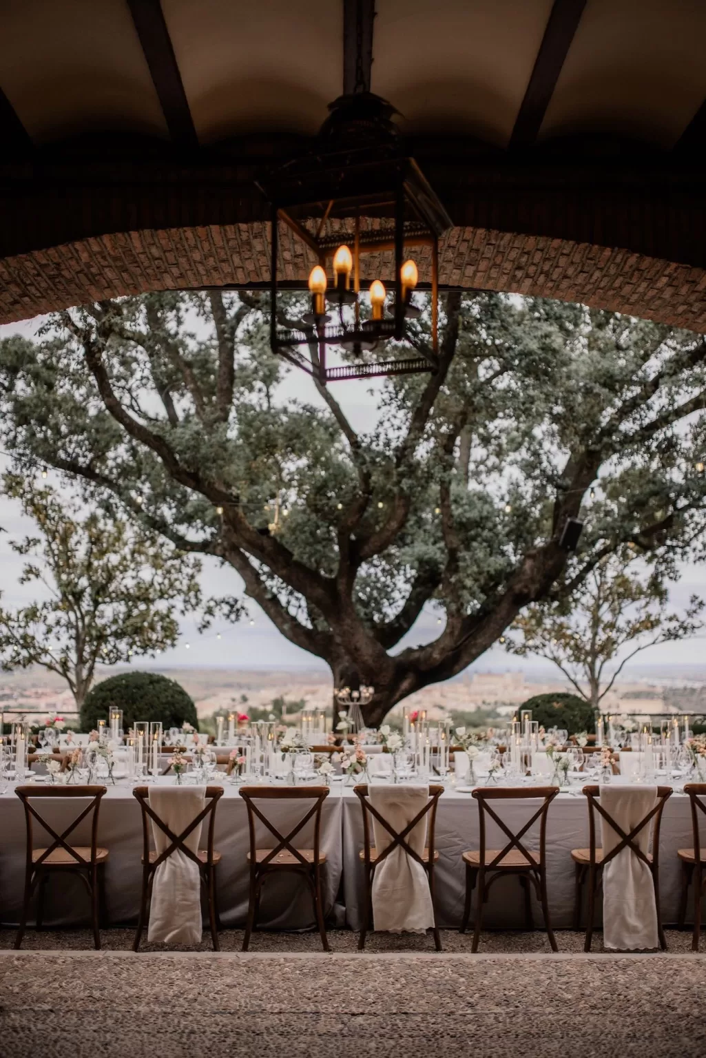 Elegant long table set for an outdoor wedding reception at Cigarral de la Mercedes, framed by trees and distant hilltop views.