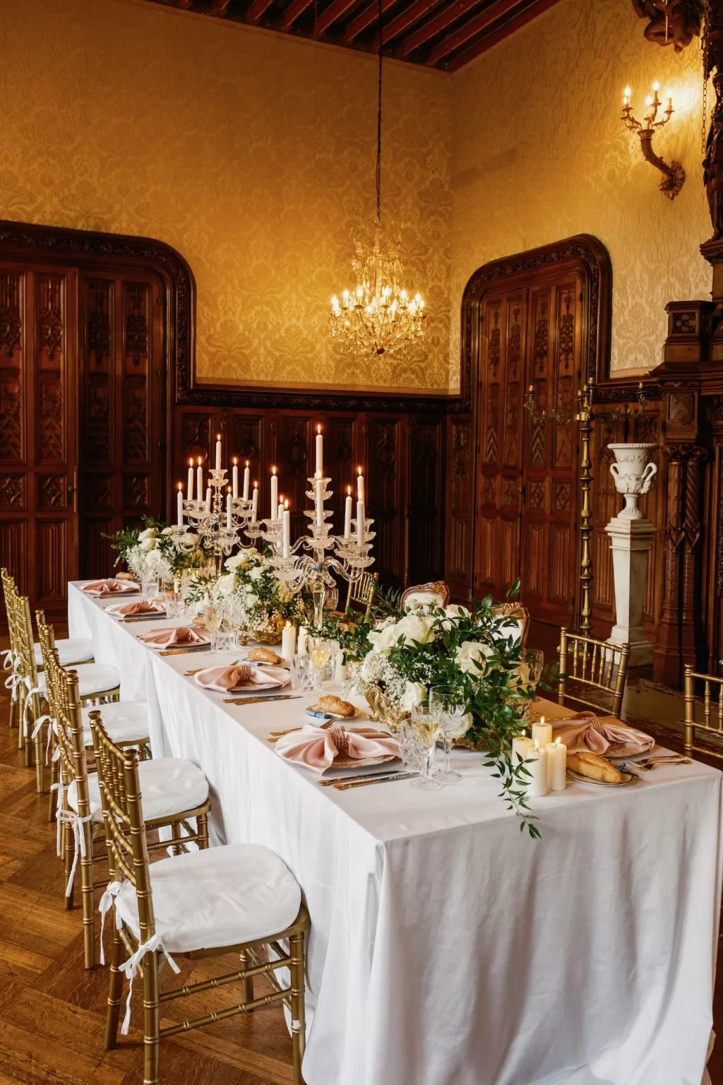 Elegant wedding tablescape with florals, candles and gold chairs inside Château Challain.