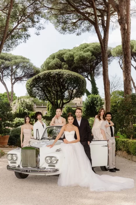 Editorial-style bridal party portrait around a vintage white car in a lush Italian garden, by The Duo Photography.