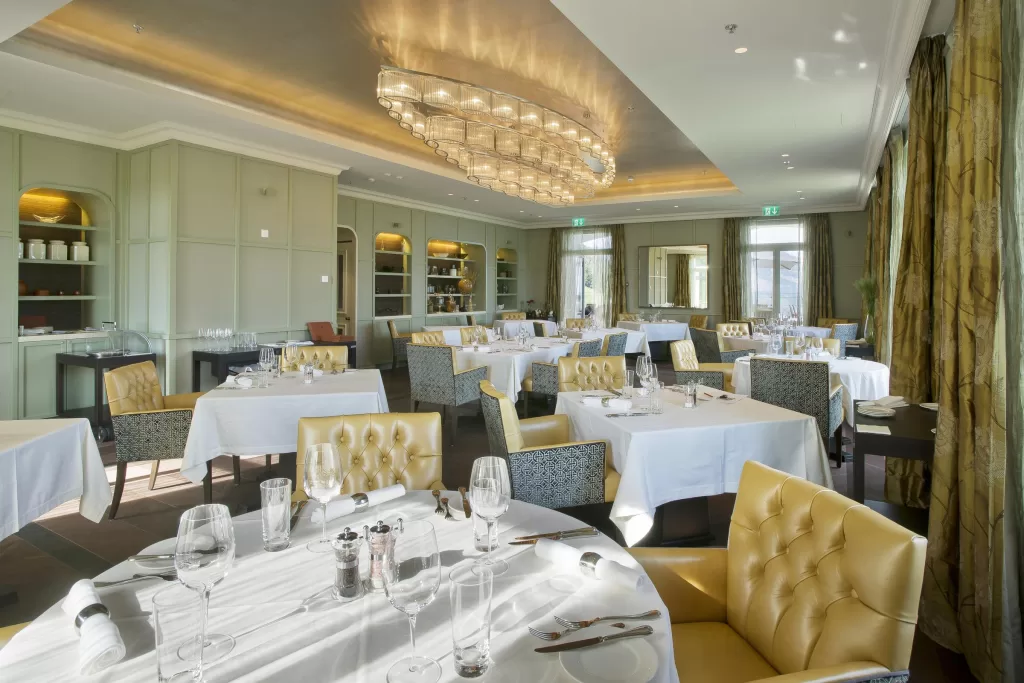 Refined dining room at Hotel Villa Honegg with soft lighting, crisp linens, and panoramic windows.