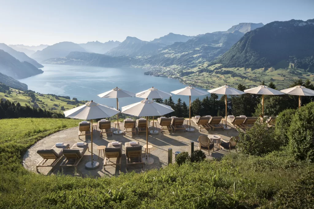 Sun loungers and white umbrellas on the terrace of Hotel Villa Honegg with panoramic lake and mountain views.