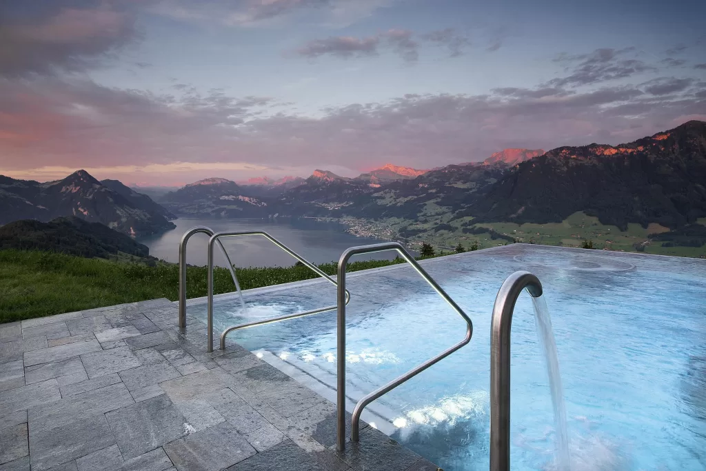 Infinity pool at Hotel Villa Honegg at sunrise with panoramic views of Lake Lucerne and snow-dusted Alps.