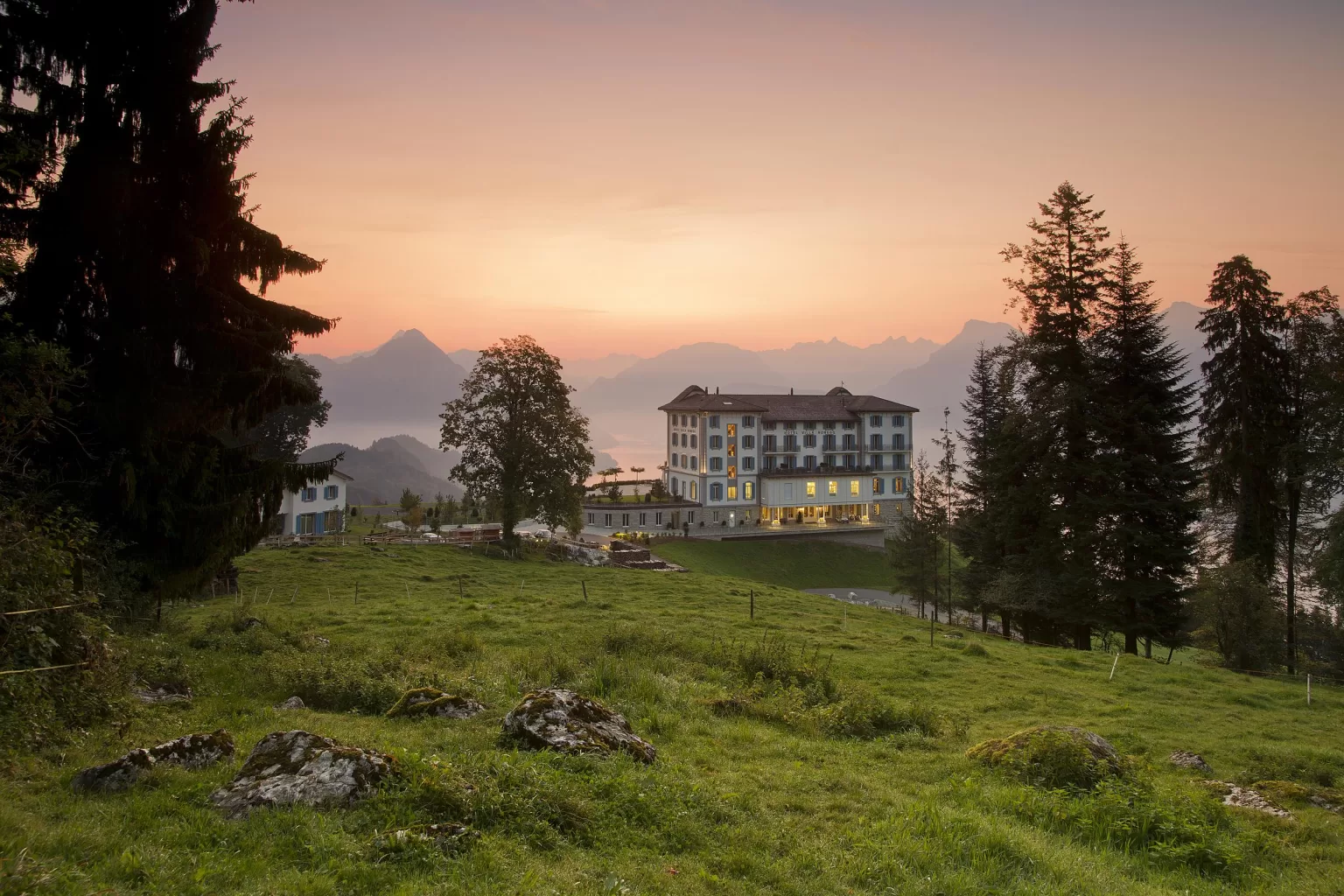 Hotel Villa Honegg at golden hour, nestled in alpine meadows with peaks silhouetted in the distance.