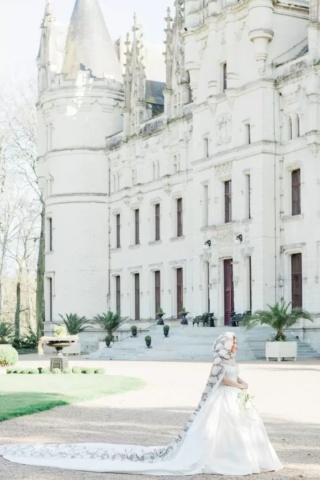 A bride in a dramatic cape-train walks before an ornate château facade, her silhouette softly lit in a majestic frame by Wim Vanhengel.