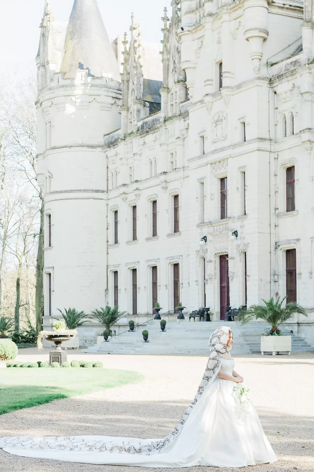 A bride in a dramatic cape-train walks before an ornate château facade, her silhouette softly lit in a majestic frame by Wim Vanhengel.