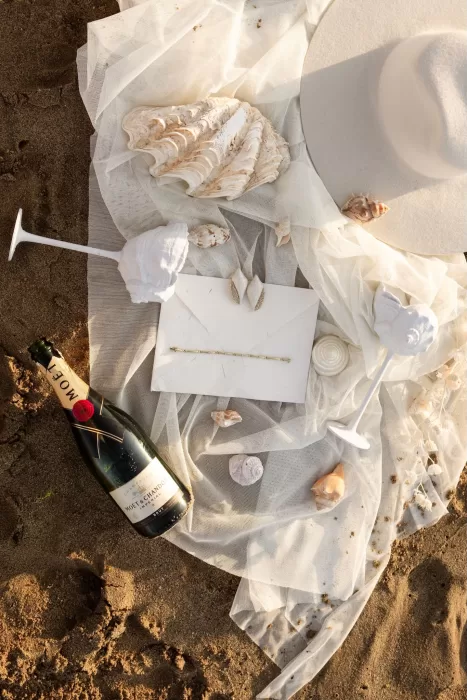 A styled flatlay of wedding details—shells, Moët bottle, and veil—laid gently on golden sand.