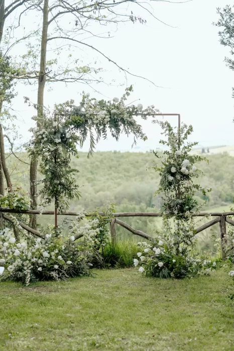 Asymmetrical floral arch with white blooms and Tuscan countryside view at Borgo Sant'Ambrogio ceremony site.