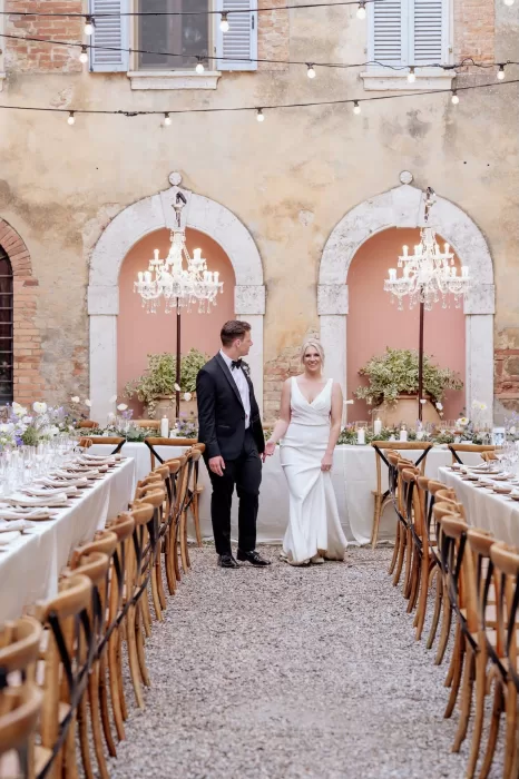 Bride and groom walk between reception tables beneath chandeliers in the courtyard of Borgo Sant'Ambrogio.