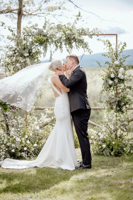 Just married couple share their first kiss under a floral arch at Borgo Sant'Ambrogio.