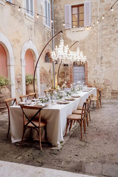Elegant outdoor reception table set in the rustic courtyard of Borgo Sant'Ambrogio with chandeliers and floral details.
