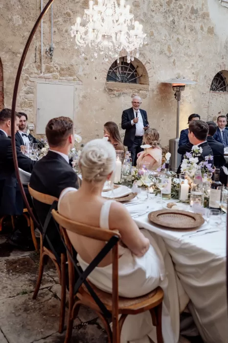 Wedding guest giving a heartfelt speech under chandeliers during dinner at Borgo Sant'Ambrogio.