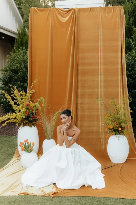 Bride sits in full gown on golden velvet at ceremony altar space at The Bradford NC.