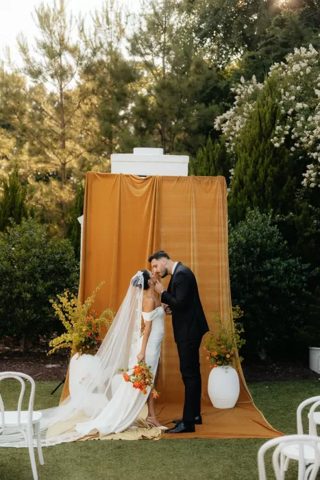 Bride and groom share a kiss in front of a mustard velvet altar backdrop at The Bradford NC.