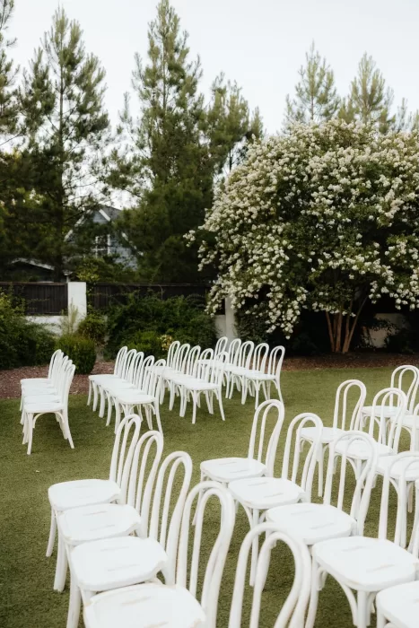Rows of classic white ceremony chairs on green lawn surrounded by trees at The Bradford NC.