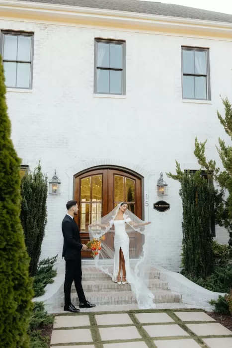 Bride twirls her veil on the front steps of The Bradford NC while groom watches.